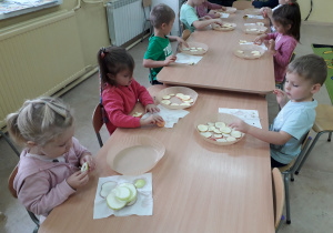 Dzieci przy stoliku wykonują susz jabłkowy, układają plastry jabłek na pergaminie.
