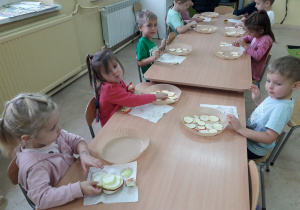 Dzieci przy stoliku wykonują susz jabłkowy, układają plastry jabłek na pergaminie.