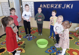 Dzieci wrzucają grosze do miski z wodą by zacząć andrzejki.