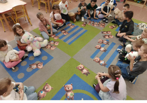 Dzieci siedzą w kole i trzymają swoje misie. Przed nimi misiowe obrazki ułożone z części.