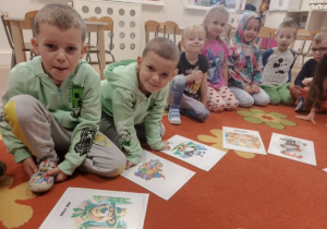 Dzieci siedzą na dywanie, przed nimi leżą obrazki ze znanymi misiami z bajek.