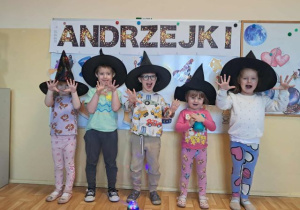Dzieci w czarnych kapeluszach pozują do zdjęcia, w tle napis andrzejki.