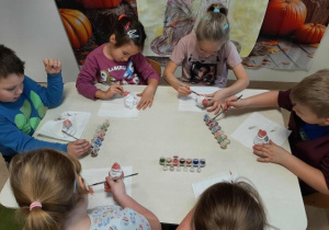 Dzieci siedzą przy stoliku i malują ceramiczne skarbonki w kształcie Mikołaja.