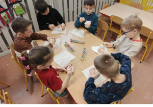 Dzieci siedzą przy stoliku i malują ceramiczne skarbonki Mikołaje