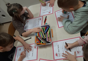 Kolejna grupa dzieci siedzi przy stoliku w sali przedszkolnej, rysują kredkami na kartce wymarzone prezenty.