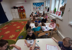 Dzieci z grupy 5, 6 latków siedzą przy stolikach rysując wymarzone prezenty.