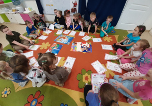 Dzieci z grupy 5, 6 latków siedzą na dywanie w kole prezentując swoje rysunkowe listy do mikołaja.