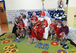 Dzieci pozują do zdjęcia z Mikołajem siedzącym w fotelu.