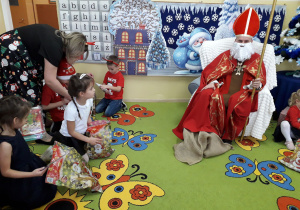 Dzieci rozpakowują prezenty od Mikołaja. W tle siedzi Mikołaj w stroju biskupa z Miry.