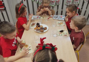 Dzieci siedzą przy stolikach i jedzą babeczki.