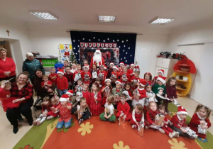 Dzieci pozują do grupowego zdjęcia z Mikołajem.