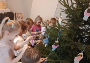 Dzieci na przedszkolnym korytarzu wieszają ozdoby na choince.