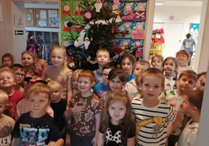 Dzieci pozują do grupowego zdjęcia, w tle pięknie ozobiona choinka.