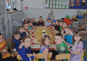 Dzieci siedzą przy złączonych stolikach przy słodkim poczestunku