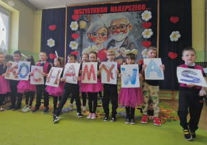 Dzieci recytują wiersze trzymając przed sobą karty z napisem KOCHAMY WAS