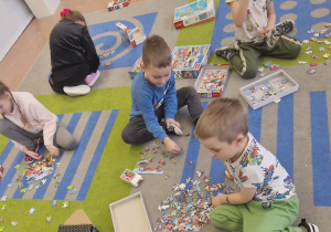 Dzieci z grupy starszaków układają na dywanie puzzle.