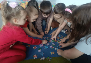 Dzieci z grupy młodszej układają na dywanie puzzle.