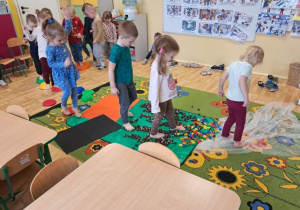 Dzieci spacerują po ścieżce sensorycznej wykonanej z kamieni sensorycznych, kasztanów, klocków i folii bąbelkowej.