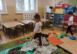 Dziewczynki spacerują po ścieżce sensorycznej wykonanej z kamieni sensorycznych, kasztanów, klocków, gazet i folii bąbelkowej.