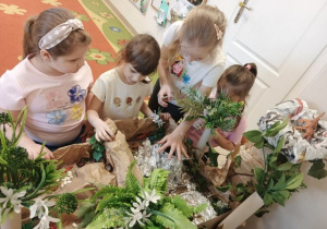 Dziewczynki bawią się figurkami dinozaurów przy makiecie parku jurajskiego.