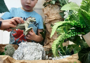 Chłopiec bawi się figurkami dinozaurów przy makiecie parku jurajskiego.