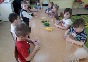 Dzieci przy stolikach przygotowują się do wykonania wody smakowej.