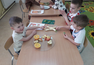 Dzieci przy stolikach tworzą owocowe kompozycje.