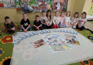 Dzieci na dywanie prezentują wykonane przez siebie plakaty "W marcu jak w garncu".