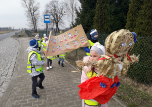 Dzieci podczas spaceru z marzanną. Chłopcy trzymają w ręku transparent "Witaj wiosno".
