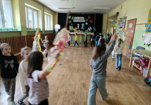 Dzieci w kole na holu przedszkolnym z gaikami śpiewają piosenkę.