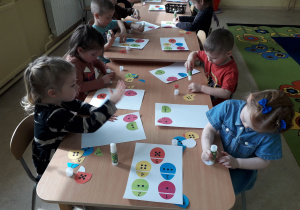Dzieci przy stolikach dopasowują i naklejają połówki pisanek.
