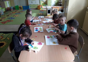 Dzieci przy stolikach dopasowują i naklejają połówki pisanek.