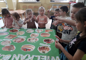 Dzieci kartonikami z nazwami podpisują potrawy wielkanocne ułożone na stole.
