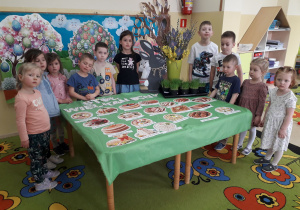 Dzieci pozują do zdjęcia wokół stołu wielkanocnego.