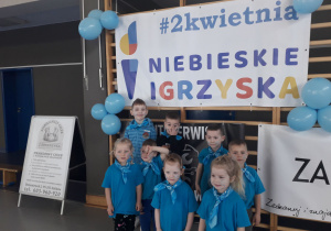 Dzieci w niebieskich koszulkach pozują do zdjęcia na tle baneru Niebieskie Igrzyska.