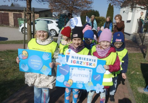 Przedszkolaki w drodze na Niebieskie Igrzyska. Dziewczynki trzymają plakaty tematyczne.