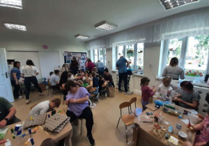 Dzieci razem z rodzicmi siedzą przy stoliku i tworzą eko zabawki