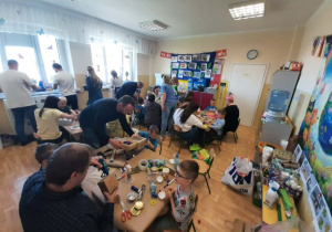 Dzieci razem z rodzicmi siedzą przy stoliku i tworzą eko zabawki