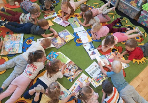 Dzieci z grupy 3,4-latków leżą na brzuszkach na dywanie i oglądają książeczki.