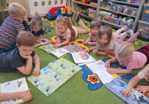 Dzieci leżą na dywanie i oglądają swoje ulubione książeczki.