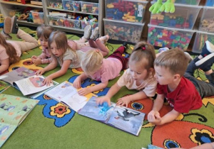 Dzieci leżą na dywanie i oglądają swoje ulubione książeczki.