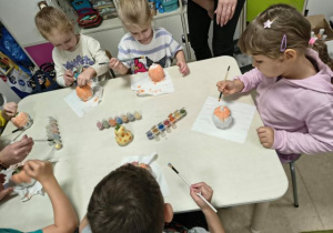 Dzieci siedzą przy stoliku i malują farabami dynie - skarbonki.