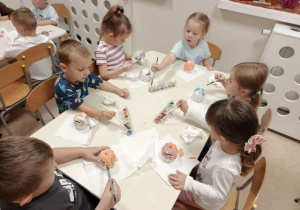 Dzieci siedzą przy stoliku i malują farabami dynie - skarbonki.