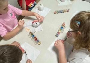 Dzieci siedzą przy stoliku i malują farabami dynie - skarbonki.