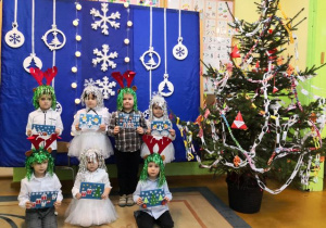 Dzieci w odświętnych ubraniach na tle bożonarodzeniowej dekoracji.