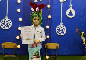 Chłopiec z dyplomem i nagrodą na tle bożonarodzeniowej dekoracji.