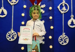 Chłopiec z dyplomem i nagrodą na tle bożonarodzeniowej dekoracji.