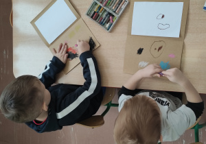 Dzieci przy stoliku malują "papierowe laptopy".