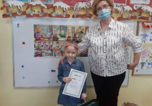 Dziewczynka trzymająca dyplom i nagrody z wychowawcą
