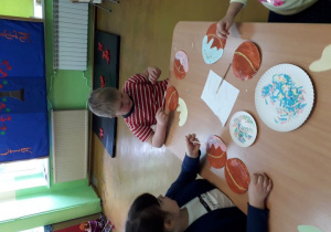 Dzieci przy stolikach dekorują pączki.